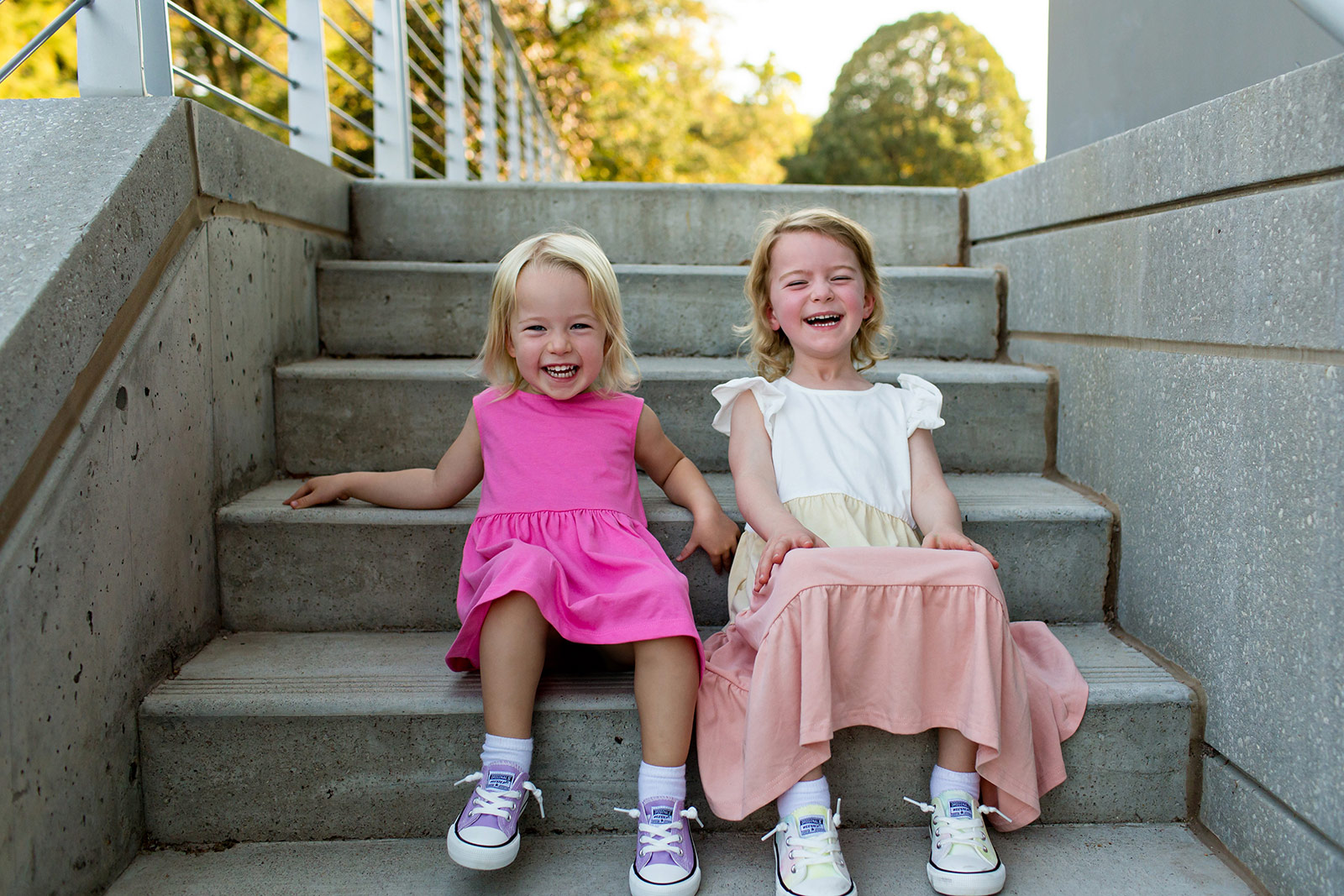 The sisters sit together on a staircase giggling.