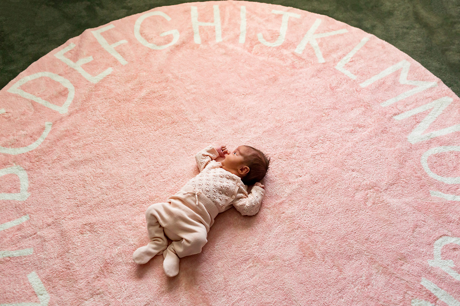 Baby Quinn lies in the middle of a large pink rug with an alphabet border.