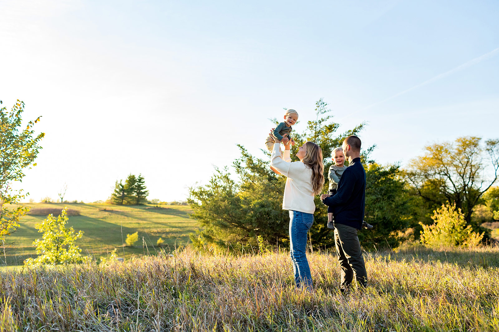 Becca holds Titus in the air as the family poses in front of beautiful rolling hills.
