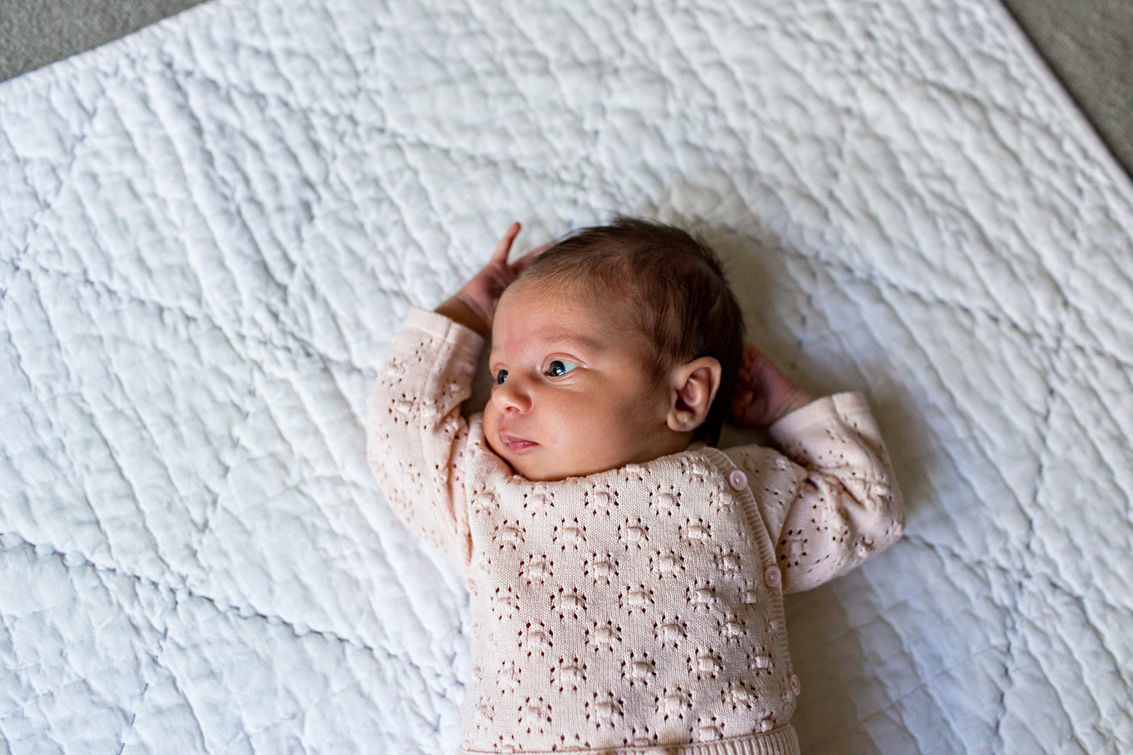 Baby Quinn, dressed in a cute sweater, lies on her quilt.
