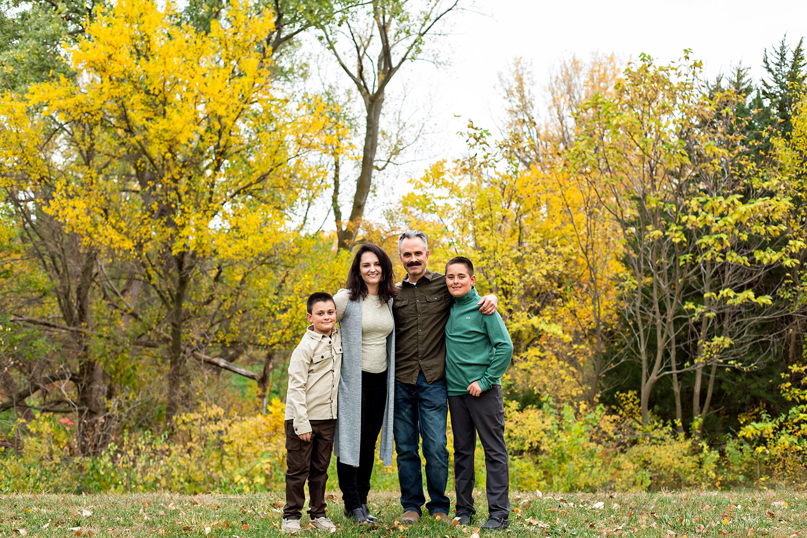 The boys stand casually with their parents in front of a beautiful mass of yellow trees..