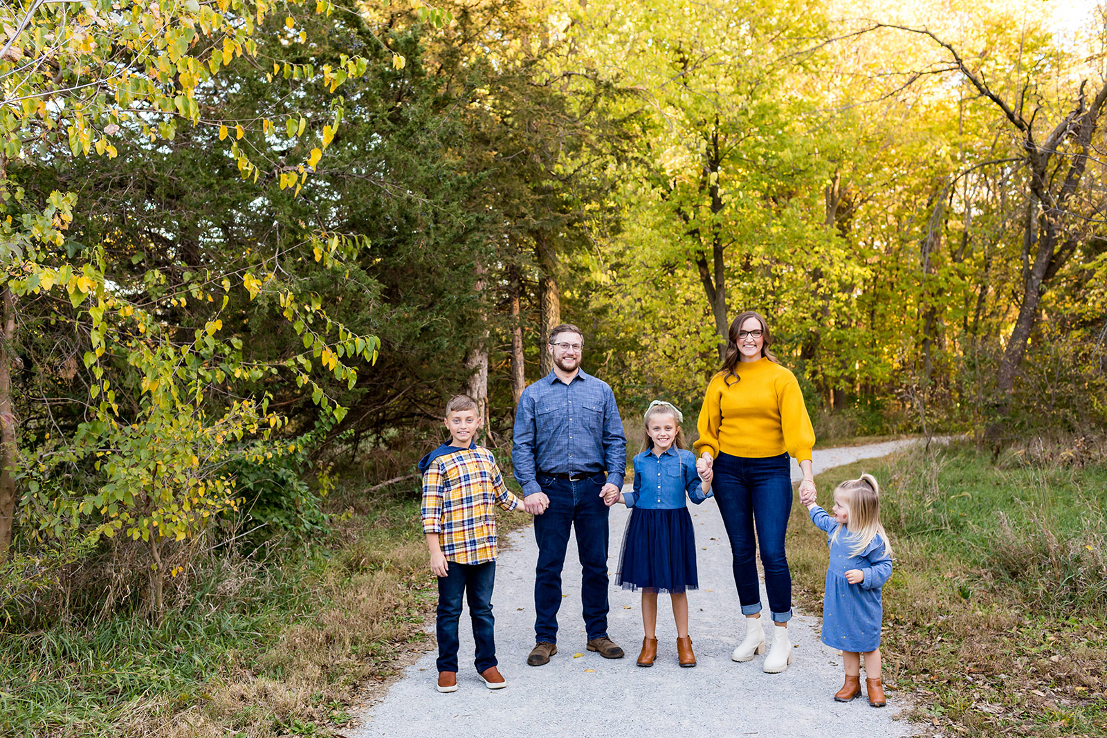 A vivid backdrop of yellow trees frames the family holding hands on a path.