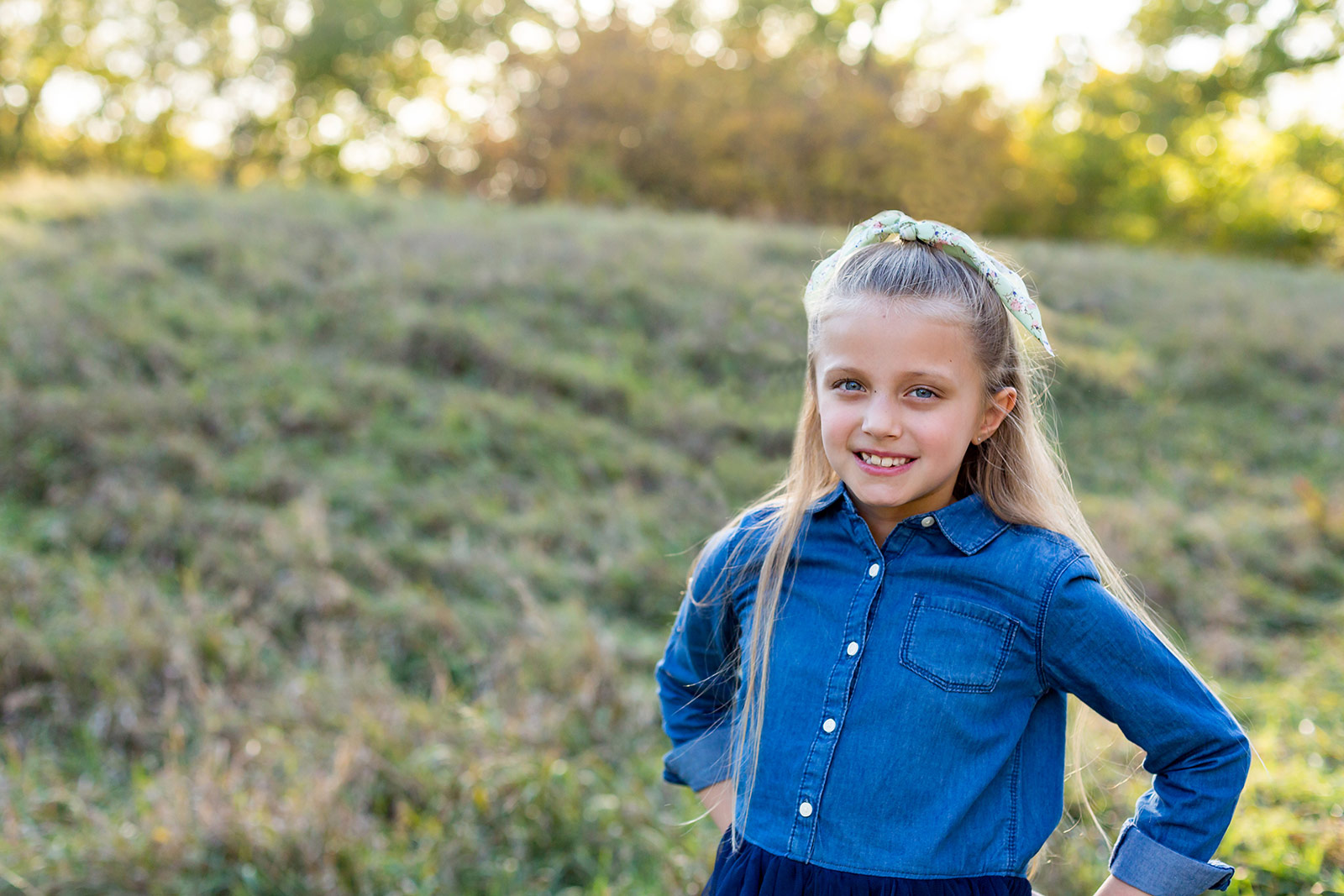 Elise smiles confidently at the camera with faded grasses and yellow trees behind her.