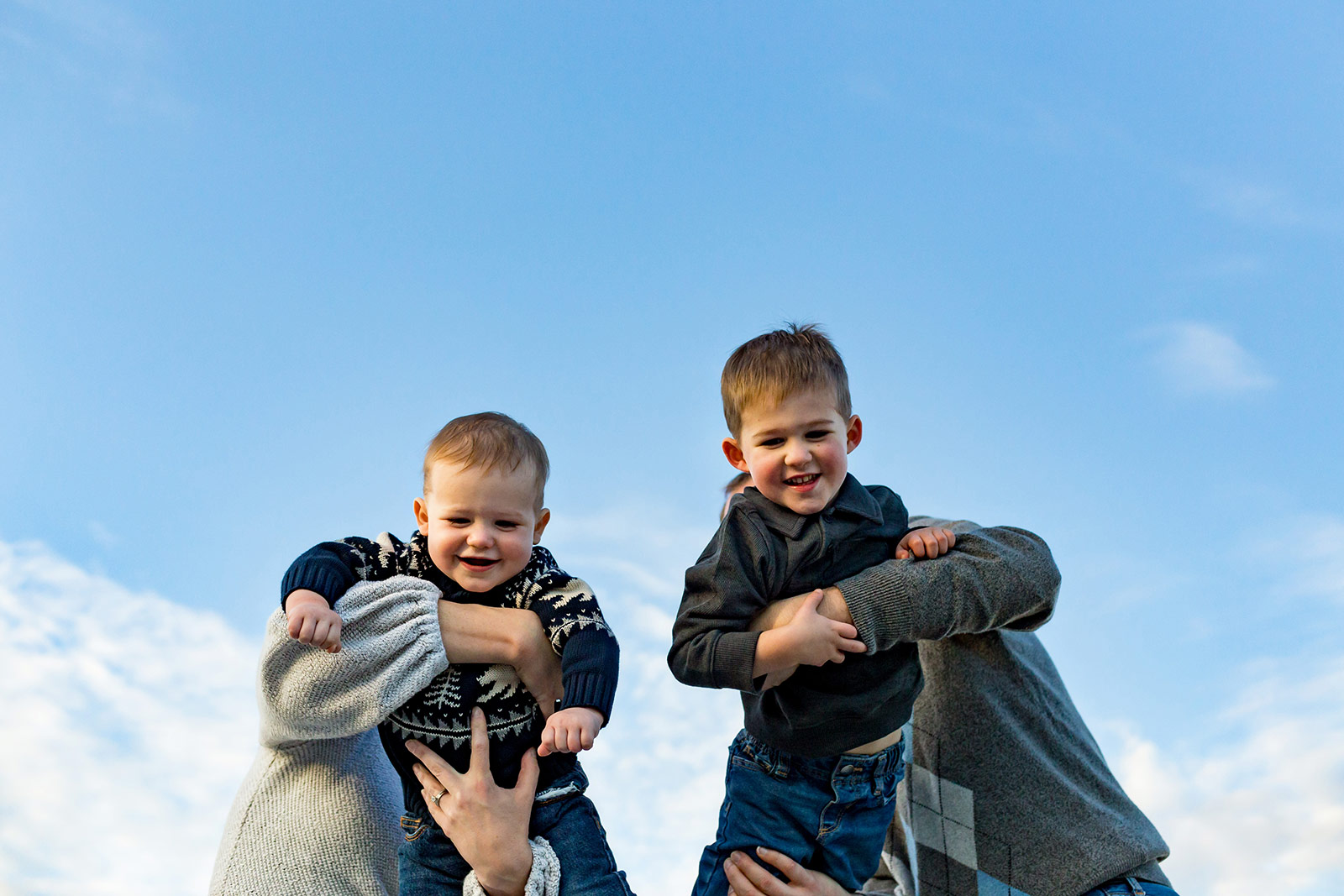 Both boys are lifted high up into the sky by their parents.