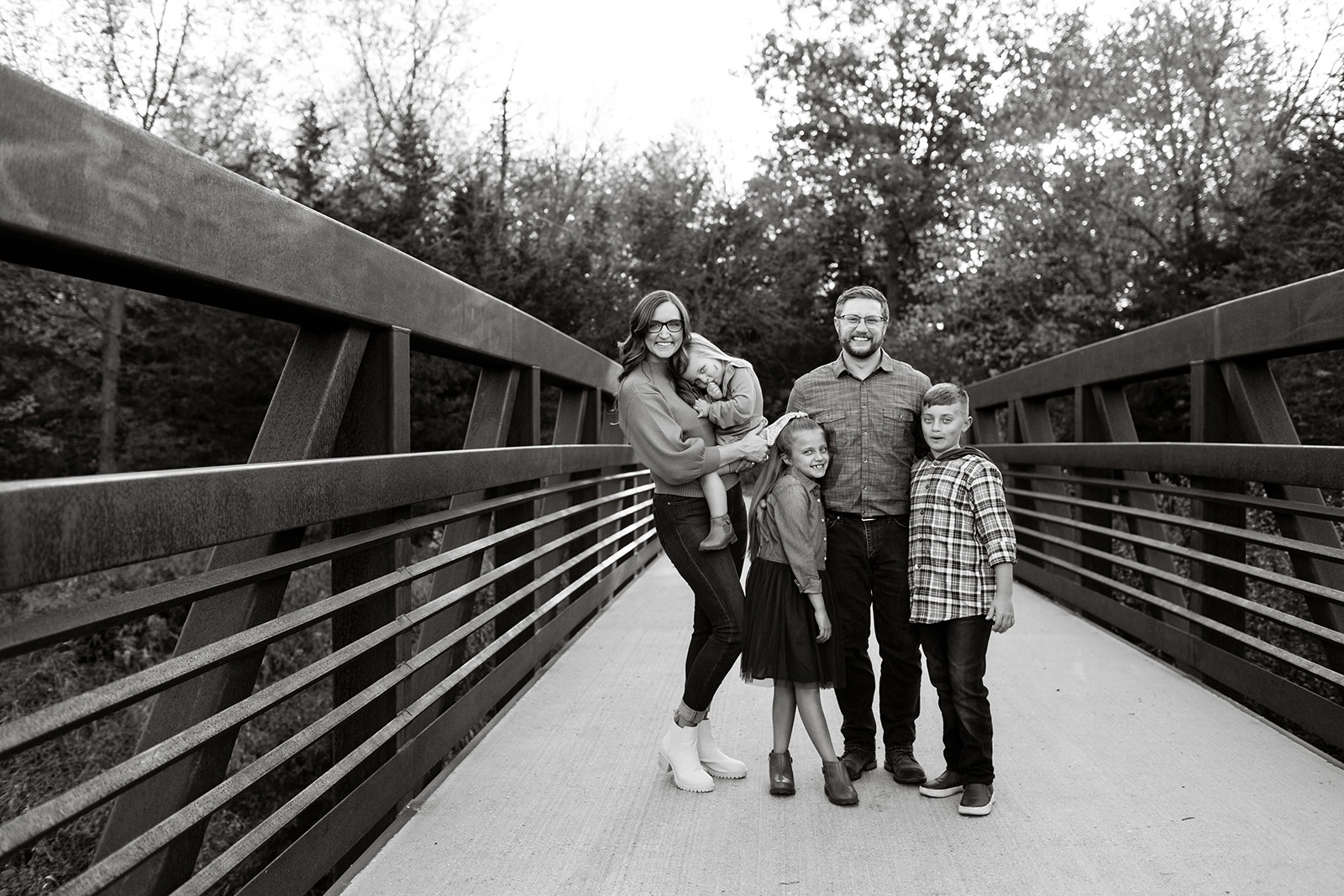 The whole family stands close together on a bridge.