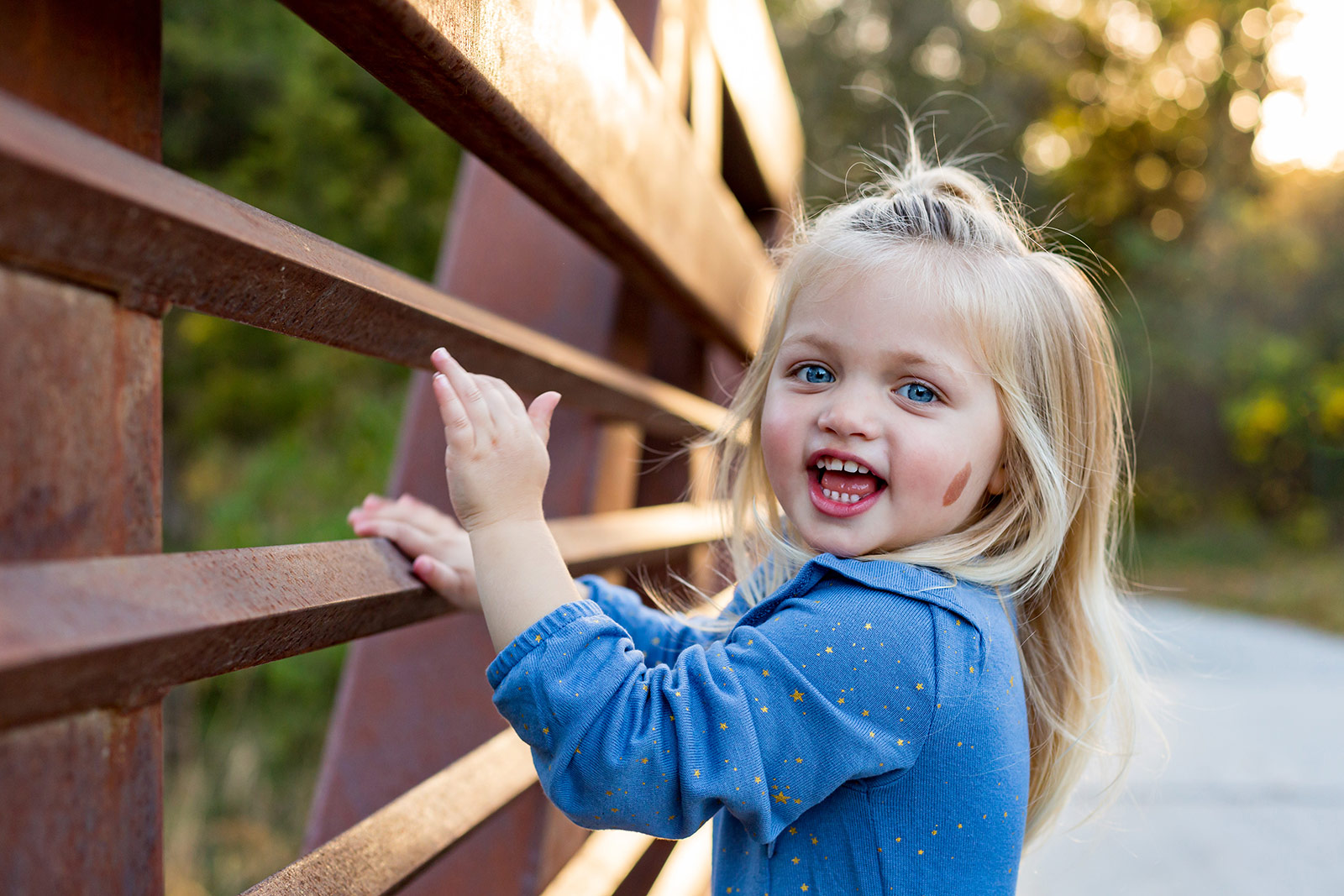 Isla plays with the rungs of the bridge railings and looks happily at the camera.