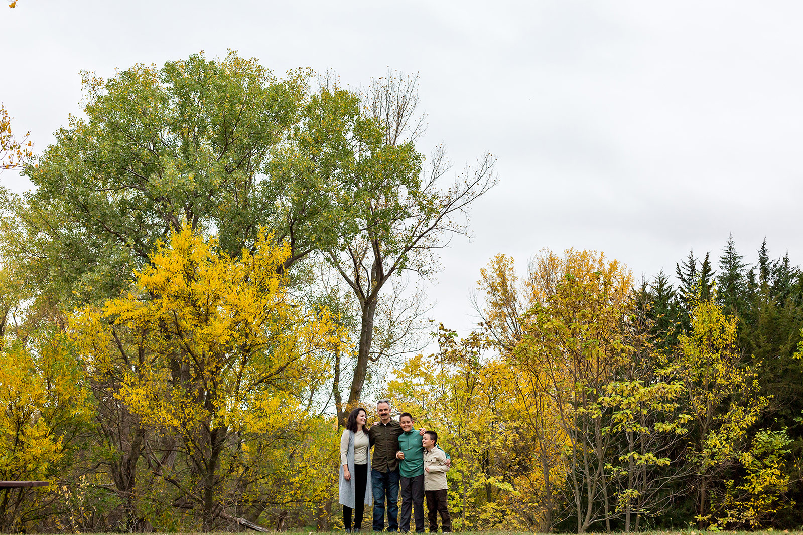 The Hassler family stands with arms linked in front of an array of fall trees.