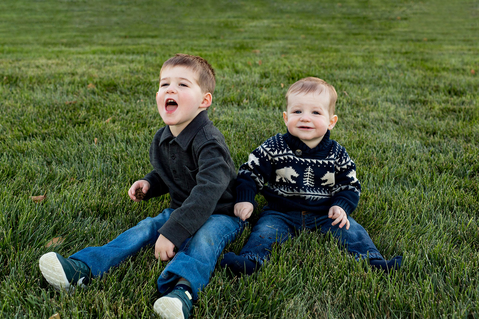 Jaxson and Beckham sit together in the grass.