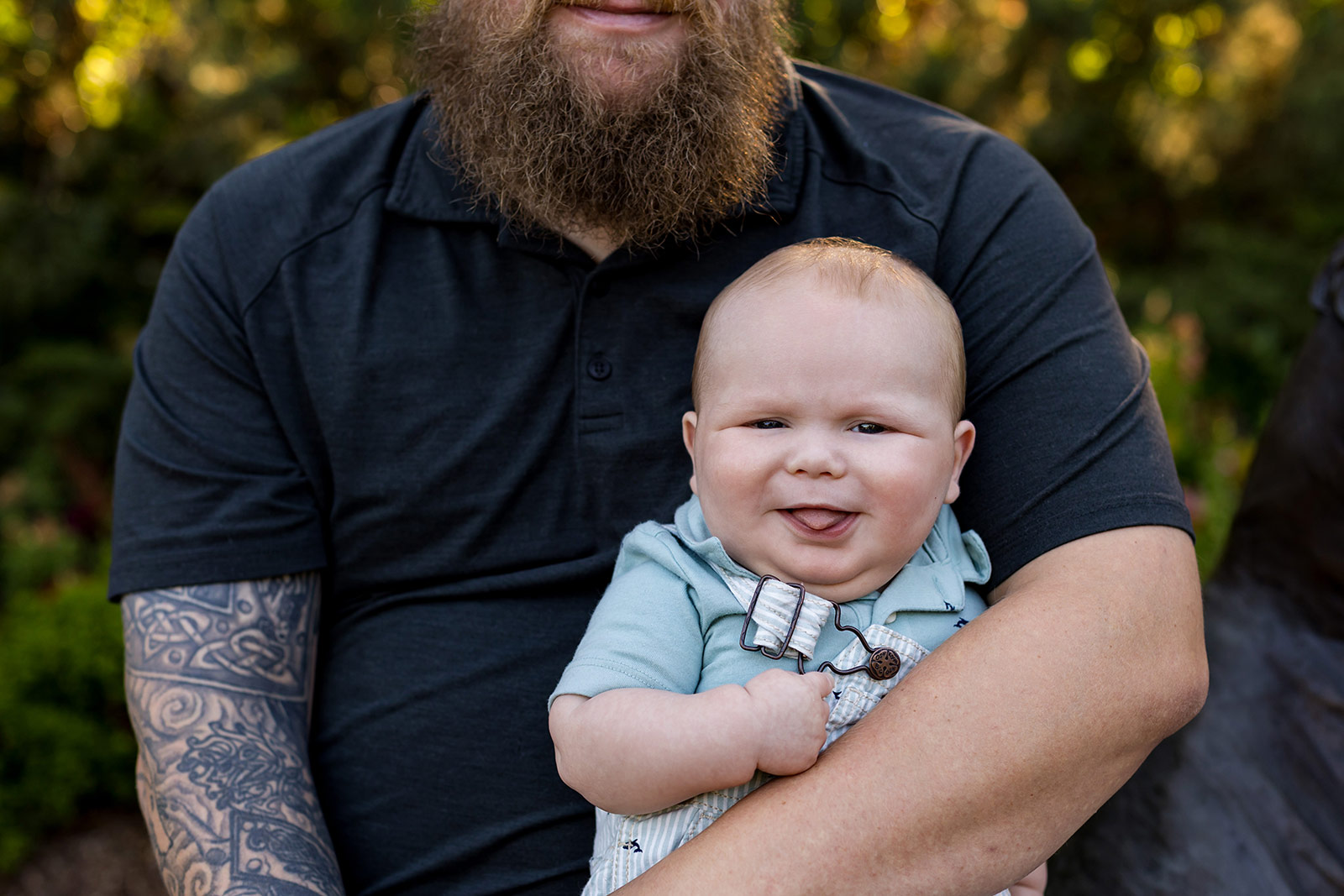 Smiling baby in light blue overalls held in a parent's arms during a colorful outdoor family photography session in Lincoln, Nebraska.
