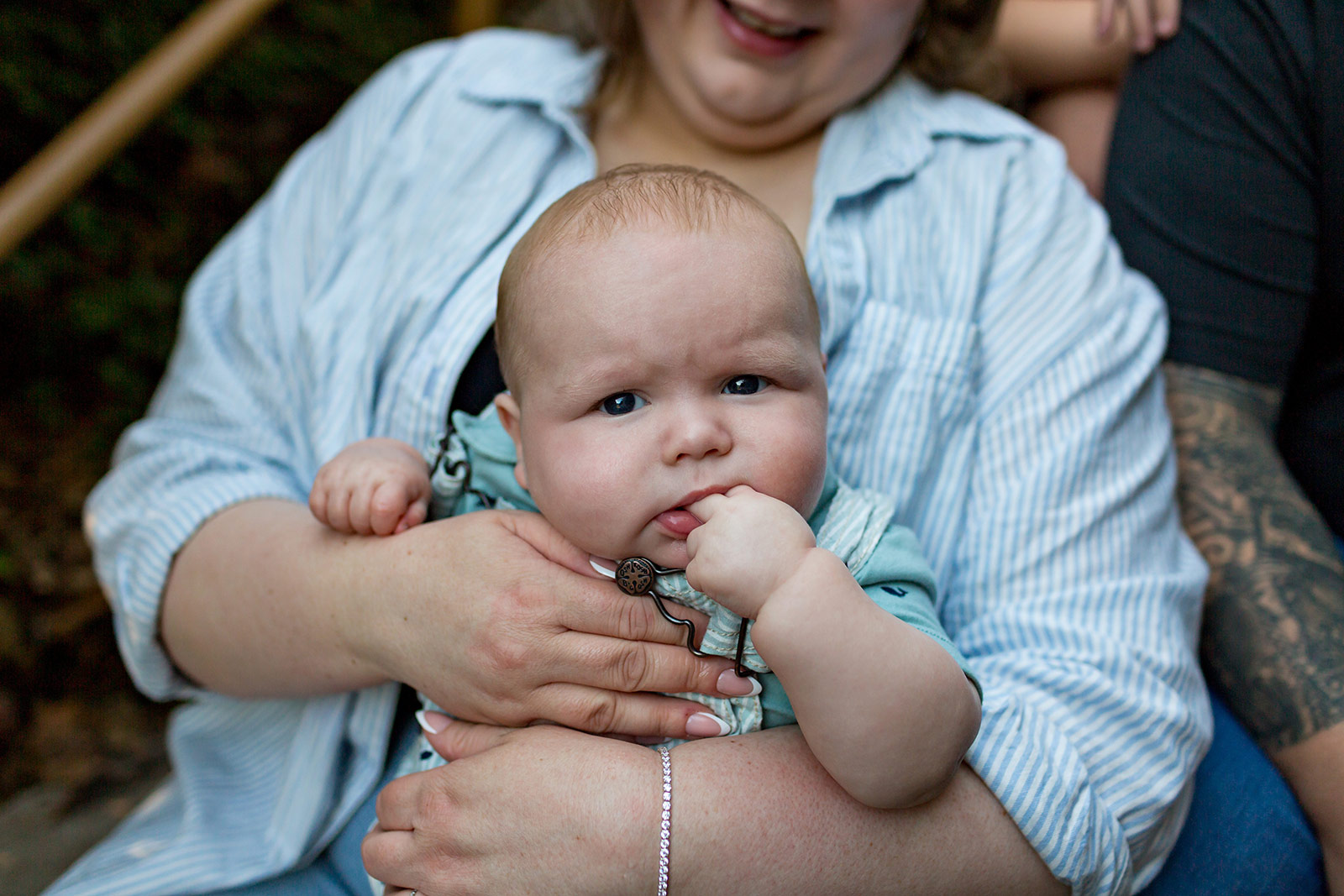 Close-up portrait of a thoughtful baby resting in mom's arms with fingers in their mouth during a relaxed family session.